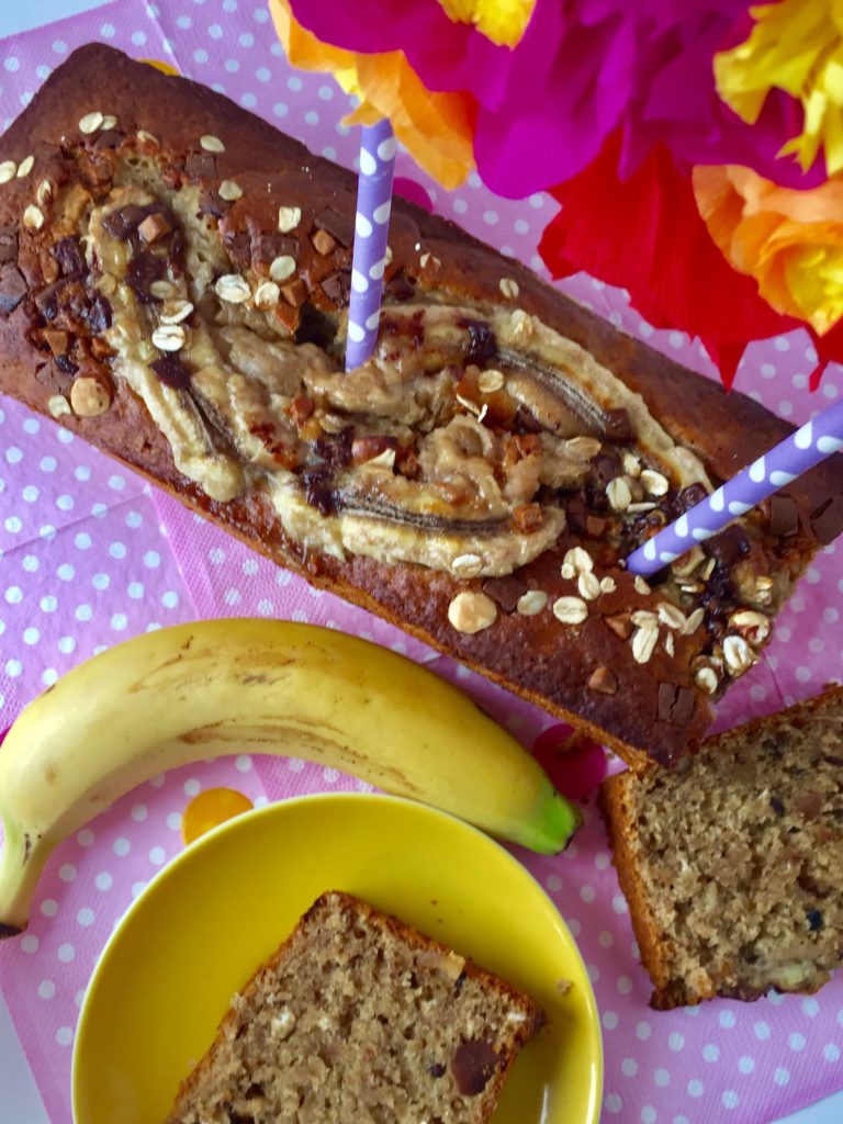 Gesundes Bananenbrot mit Karamellcrunsh mit einer Blumengirlande und einem Stück des Kuchens auf einem gelben Teller.